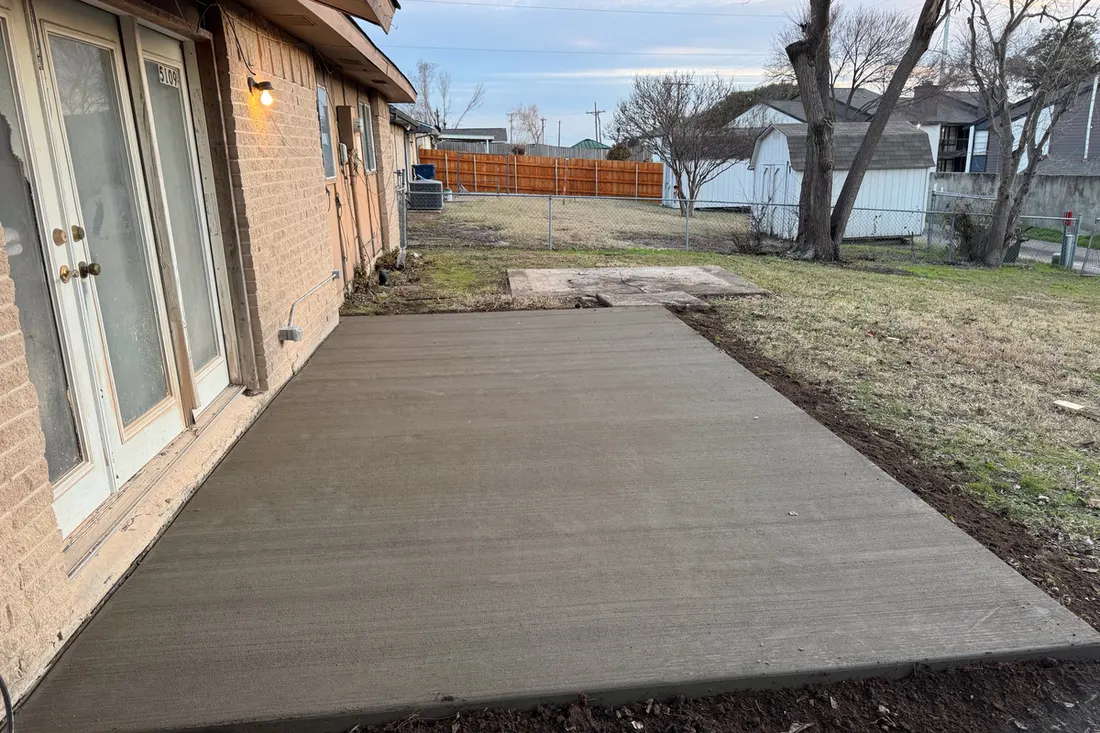 Freshly poured concrete patio slab outside the glass doors of a brick house yard