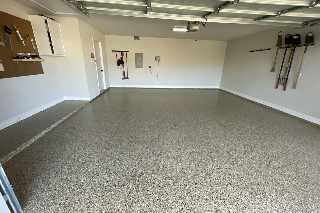 Spacious garage interior featuring glossy speckled beige and gray coated concrete flooring with light neutral walls
