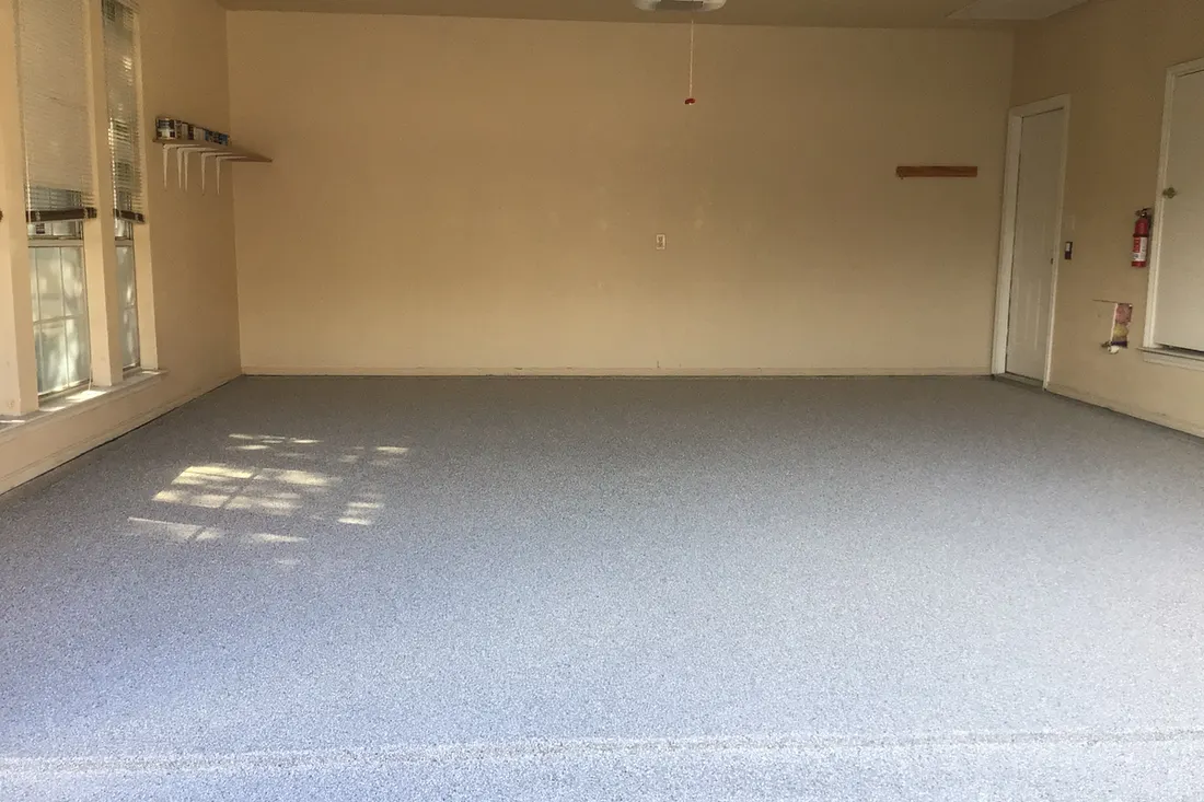 Empty garage interior featuring a gray speckled epoxy coated concrete floor and beige walls