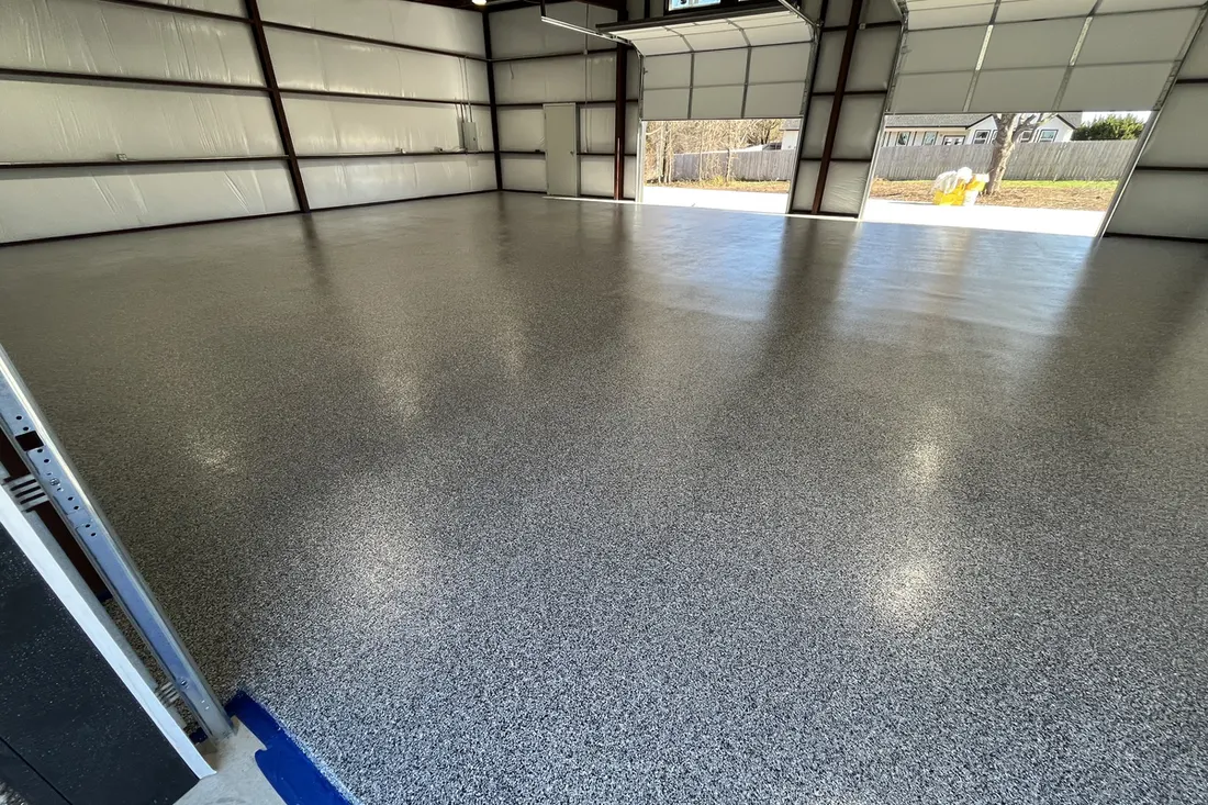 Glossy speckled gray concrete floor inside a large steel garage with open roll-up doors