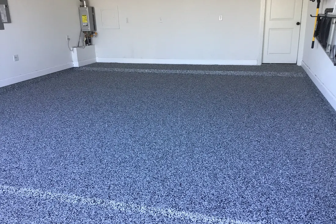 Gray and black speckled flake concrete coating across an empty garage floor with white walls