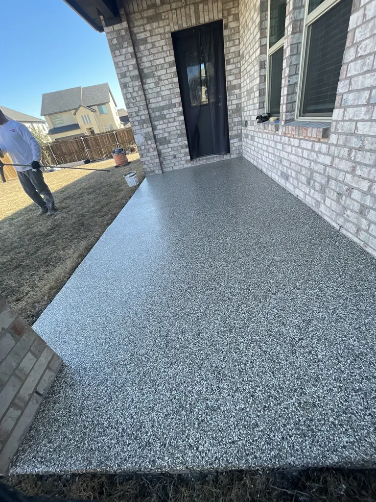 Gray speckled flake concrete coating on a covered backyard patio floor beside a brick house