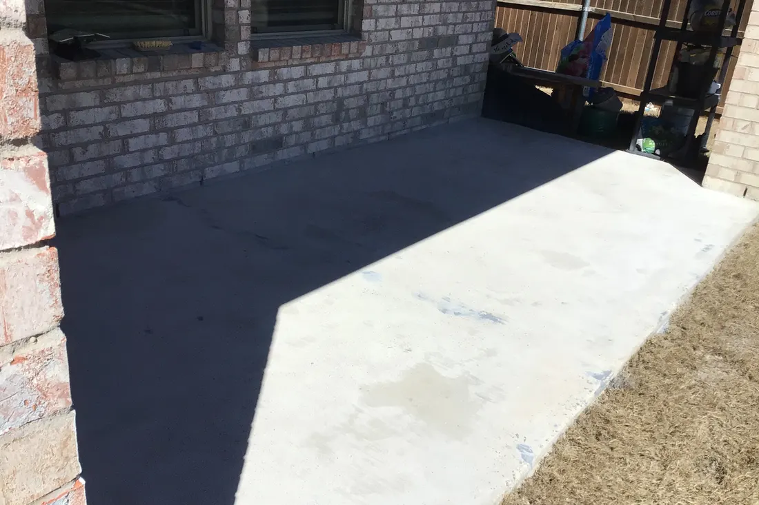 Backyard concrete patio slab partially covered in shadow next to a brick house exterior