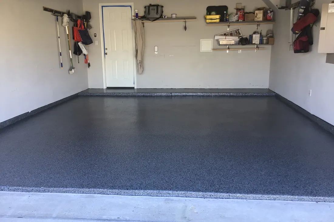 Garage interior featuring a glossy dark gray speckled epoxy coated concrete floor with baseboards