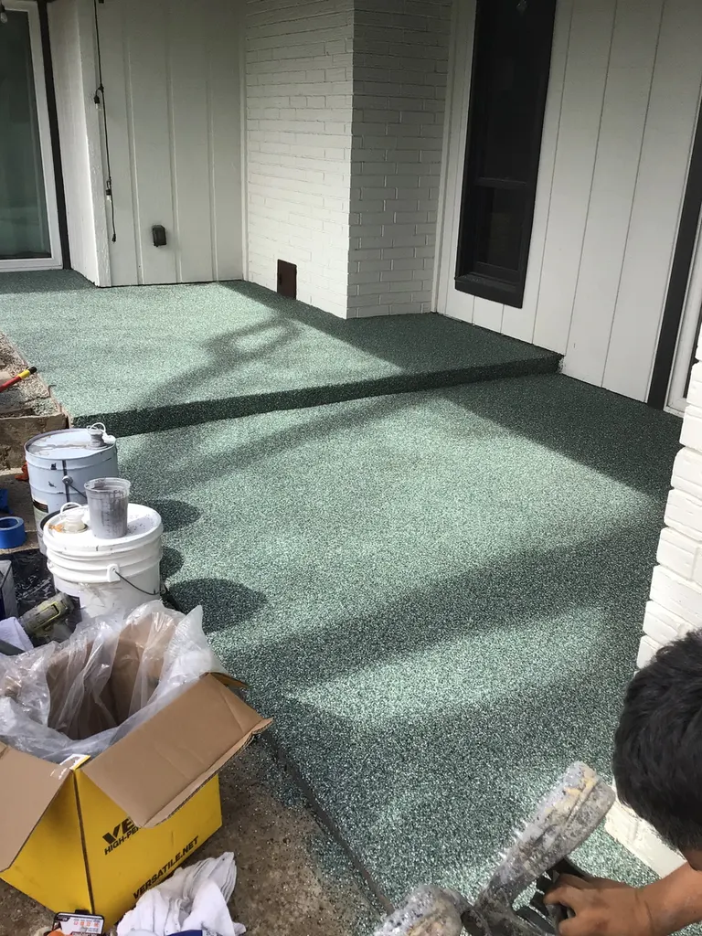 Freshly applied green speckled concrete flake coating on an outdoor patio with steps and white siding