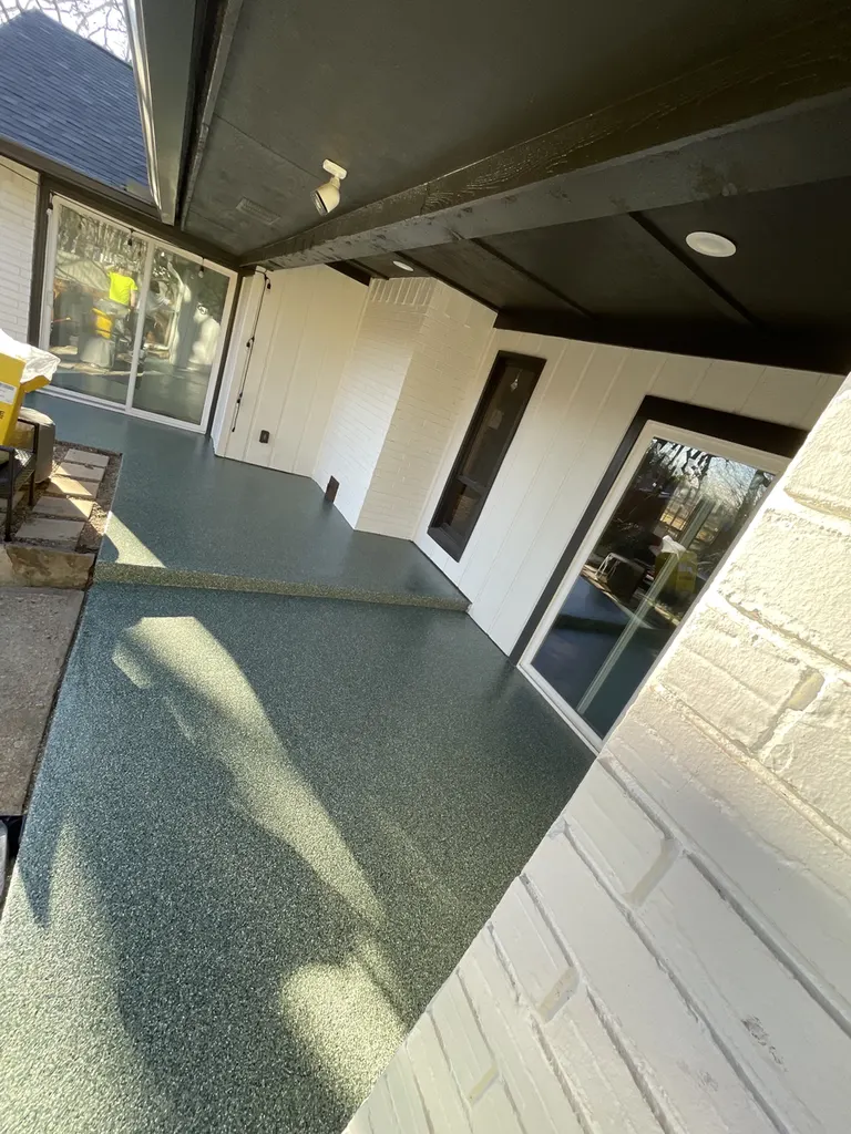 Dark speckled concrete coating on a covered residential patio beside white brick walls