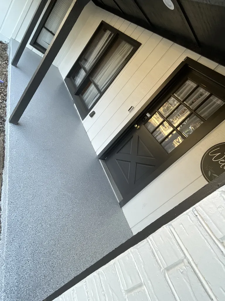 Gray speckled coated concrete porch floor outside a house with white siding and black trim