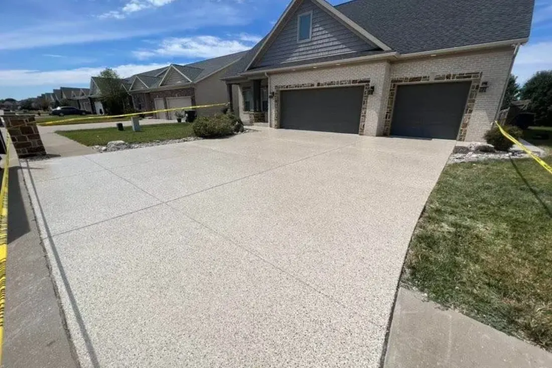 Freshly coated speckled beige concrete driveway in front of a suburban brick garage