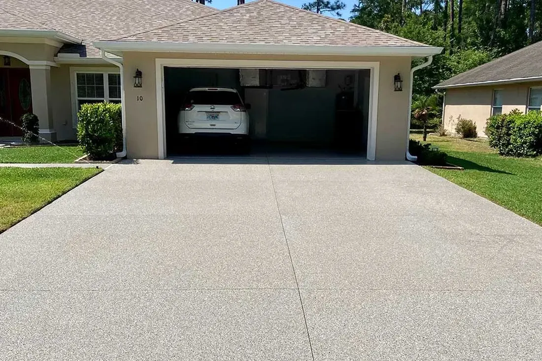 Coated light gray concrete driveway leading to an open garage of a suburban home