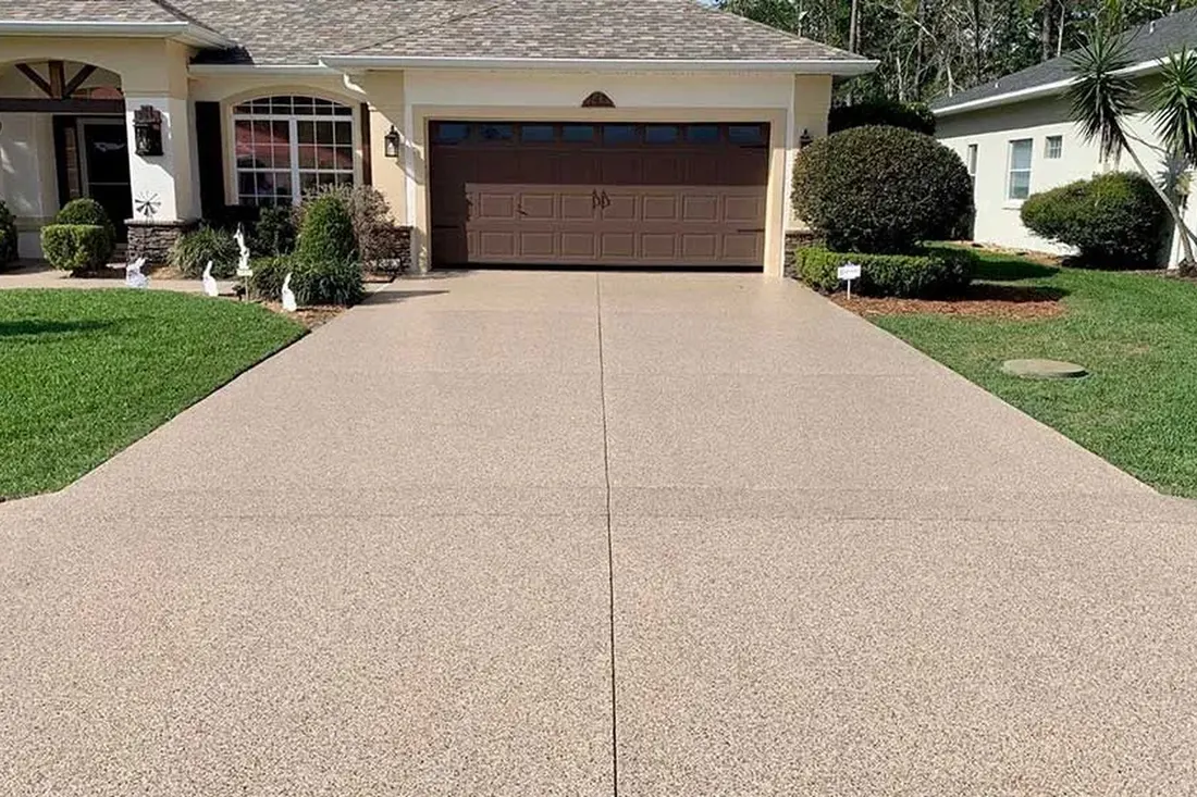 Beige speckled coated concrete driveway leading to a brown garage door between green lawns