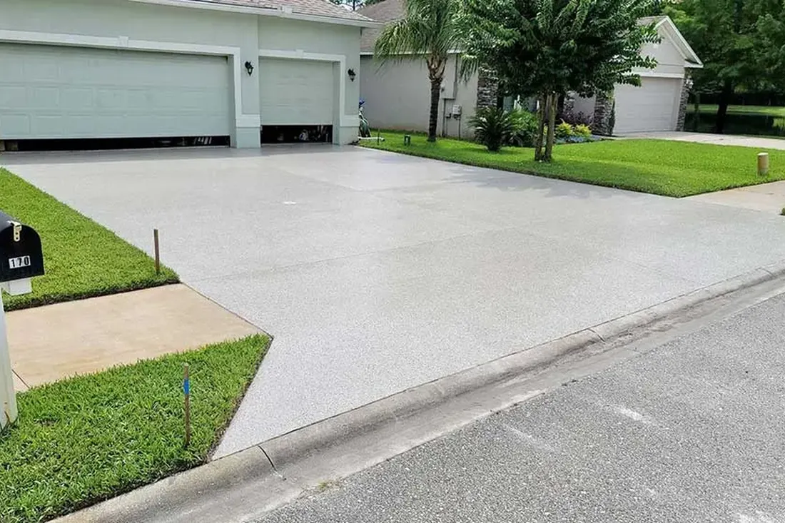 Freshly coated light gray concrete driveway leading to a suburban two-car garage flanked by green lawn