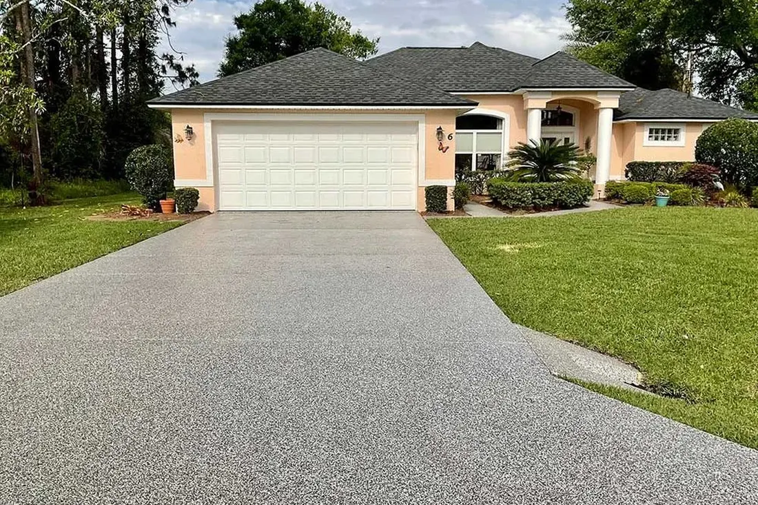 Speckled gray coated concrete driveway leading to a garage on a suburban home with green lawn