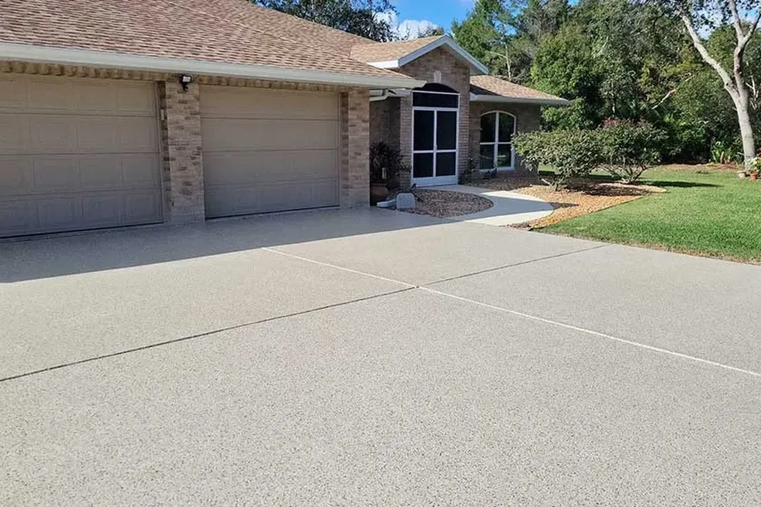 Freshly coated beige concrete driveway leading to a brick house with a two-car garage