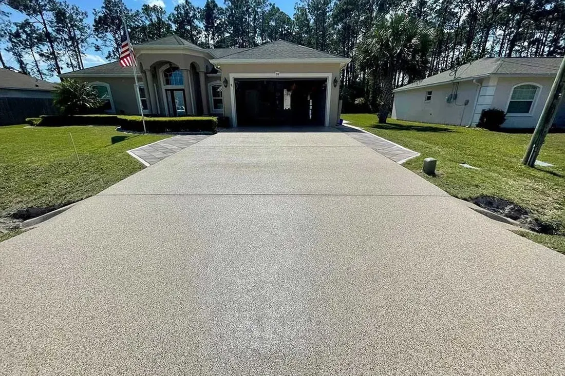 Tan textured coated concrete driveway leading to a suburban garage with brick paver borders