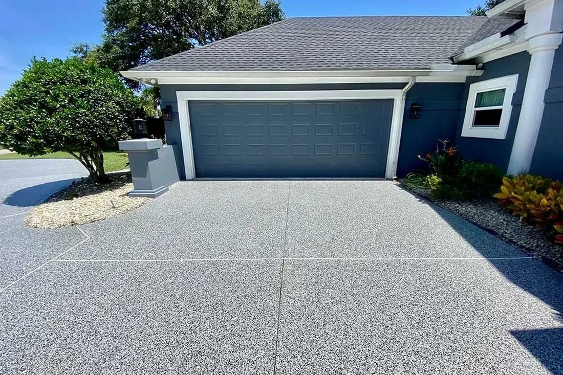 Gray speckled coated driveway leading up to a closed garage door on a blue house