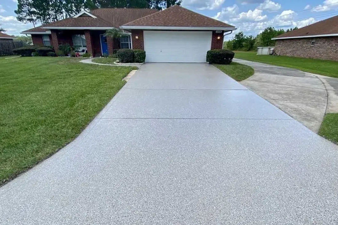 Freshly coated light gray speckled concrete driveway leading to a brick house and white garage door