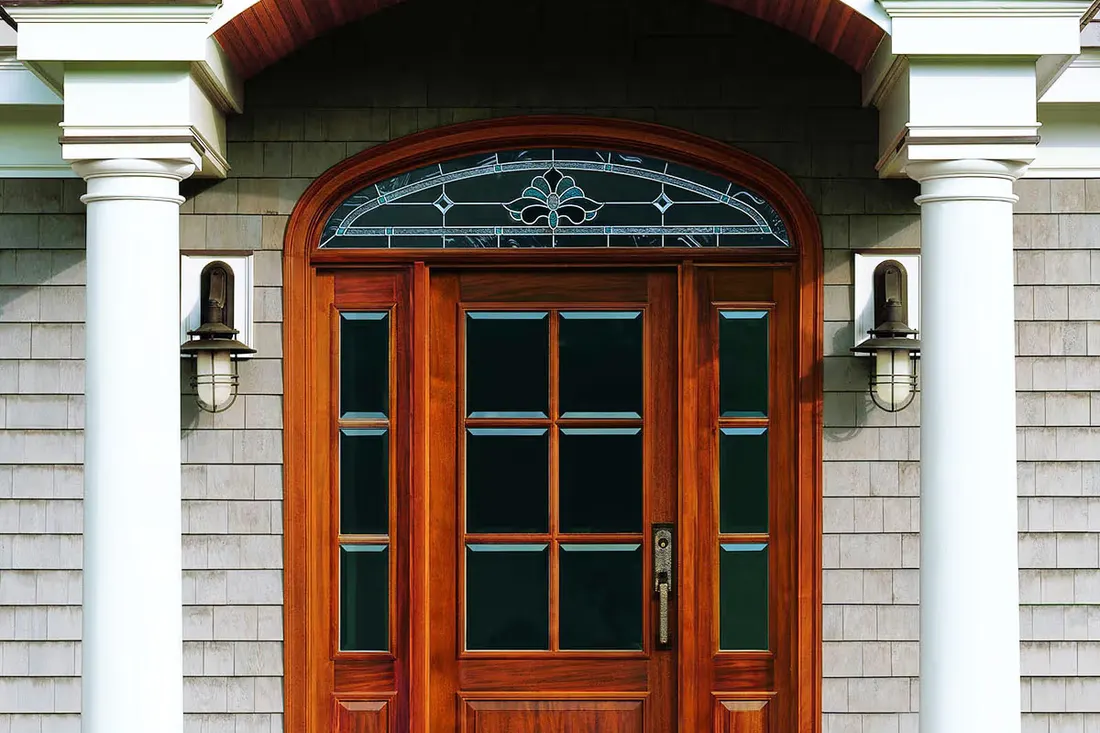 Wood front entry door with glass panes, decorative arched transom, and white porch columns