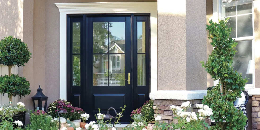 Black front entry door with glass panes and sidelights surrounded by potted porch plants