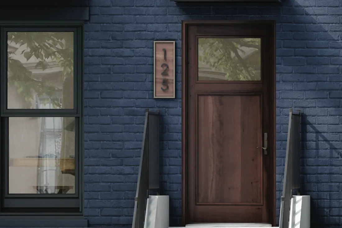 Dark wood front entry door with upper window set in blue painted brick house wall