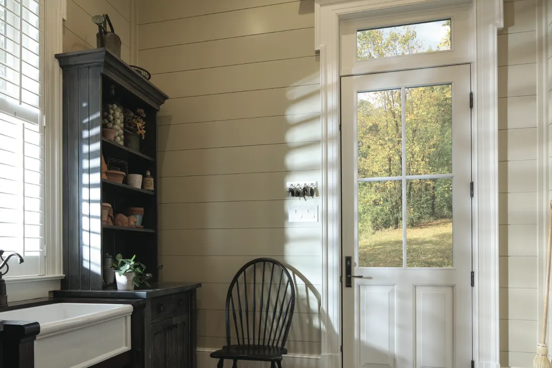 White entry door with window panes and transom in a rustic room with shiplap walls