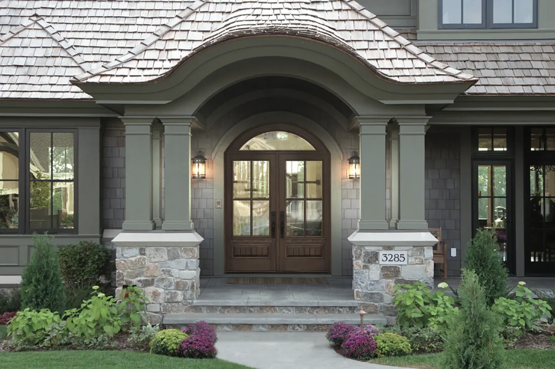 Double wood entry doors with glass panes under an arched portico with stone pillars