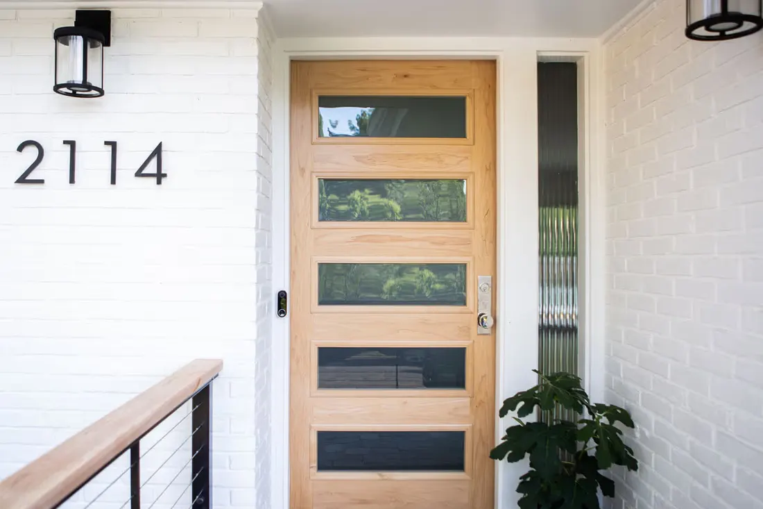 Light wood front entry door with horizontal glass panes set in a white brick exterior