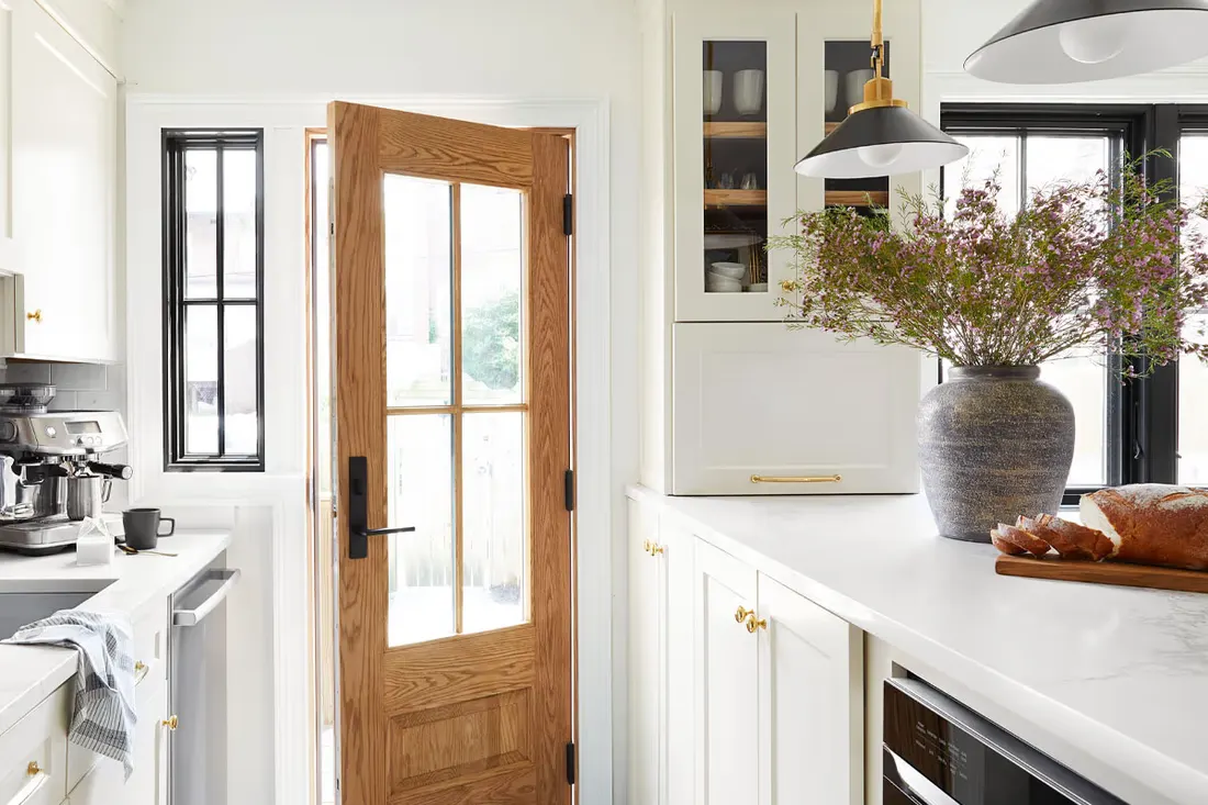 Open wood entry door with four glass panes in a bright white kitchen