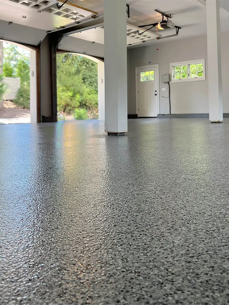 Glossy gray speckled epoxy coating on a spacious garage floor with white support pillars