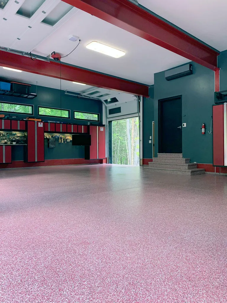 Spacious garage with pink flake coated concrete floor, teal walls, and red cabinets and beams