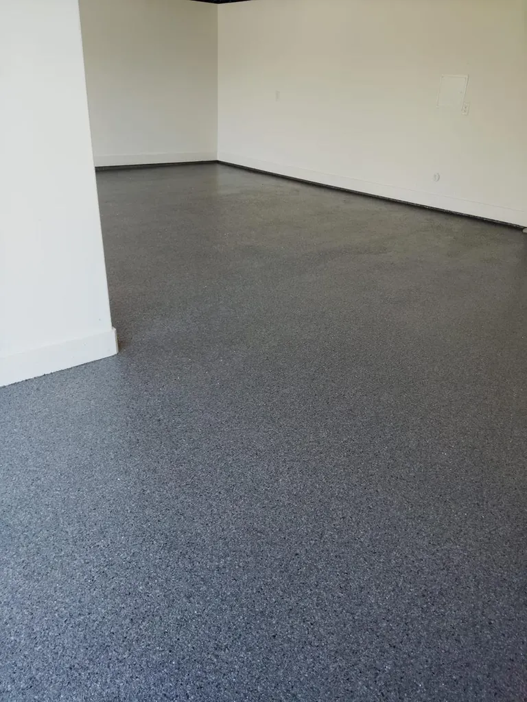 Freshly coated grey speckled epoxy flooring in an empty garage with white walls