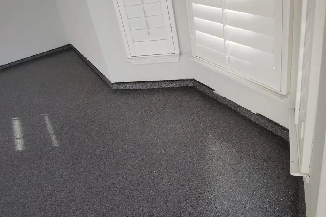 Dark gray speckled epoxy coating on a floor beside white walls with shuttered windows