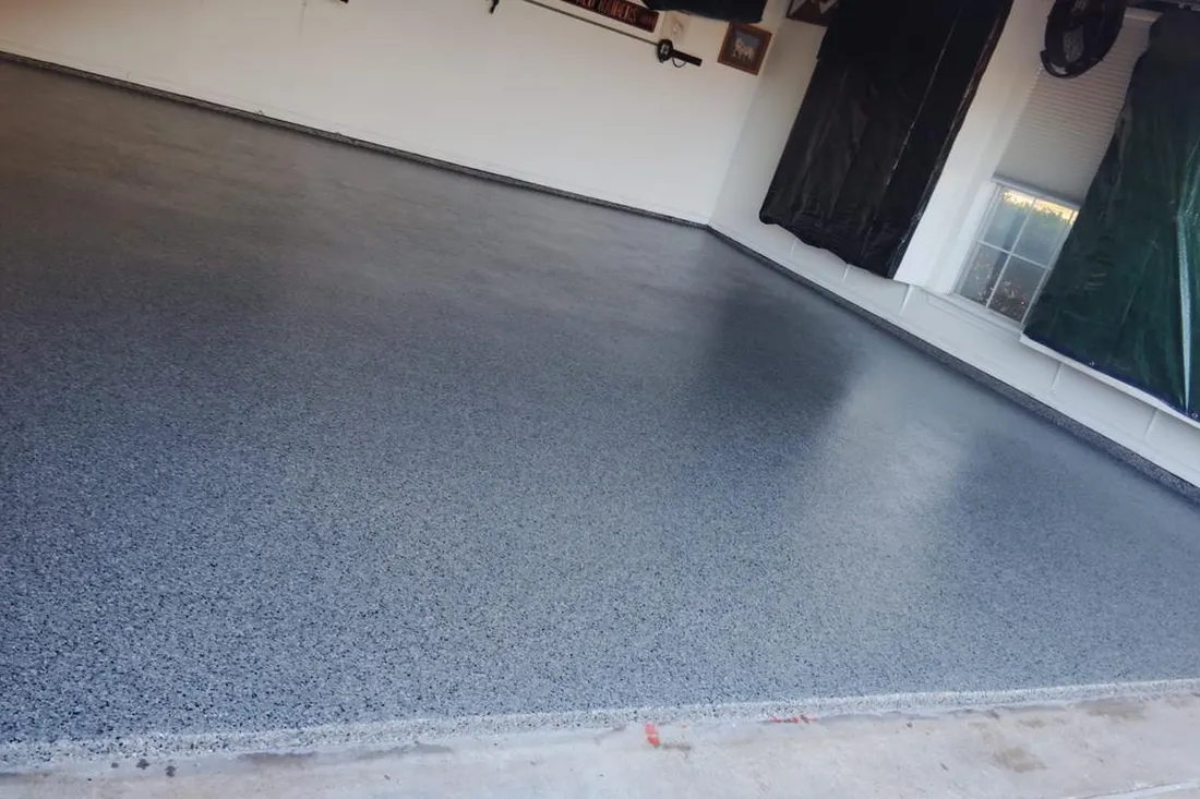 Glossy gray speckled flake coating on an empty garage concrete floor beside white walls