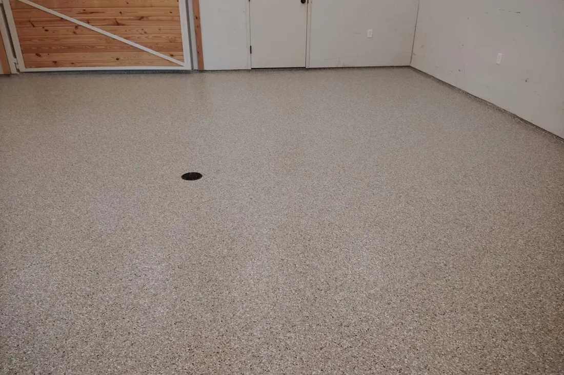 Tan speckled epoxy coated garage floor with a circular floor drain and white walls