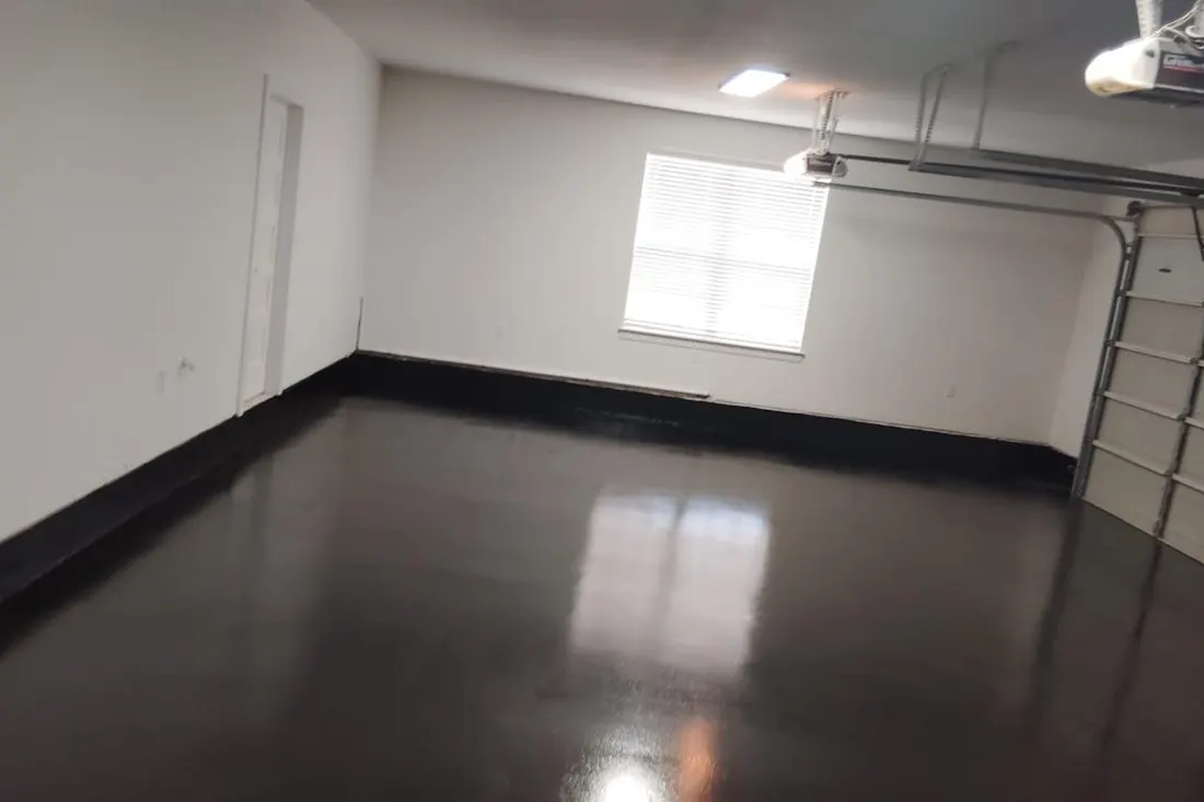 Glossy black coated floor inside an empty garage with white walls and a window