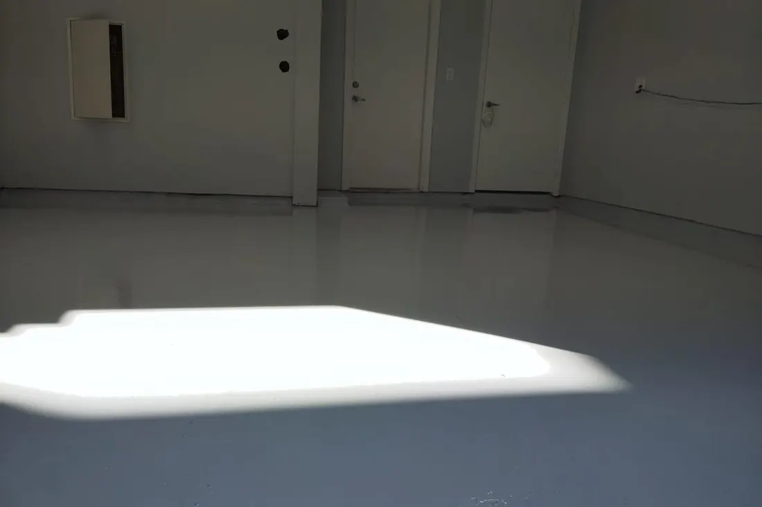 Glossy light gray epoxy coated garage floor reflecting sunlight in an empty room