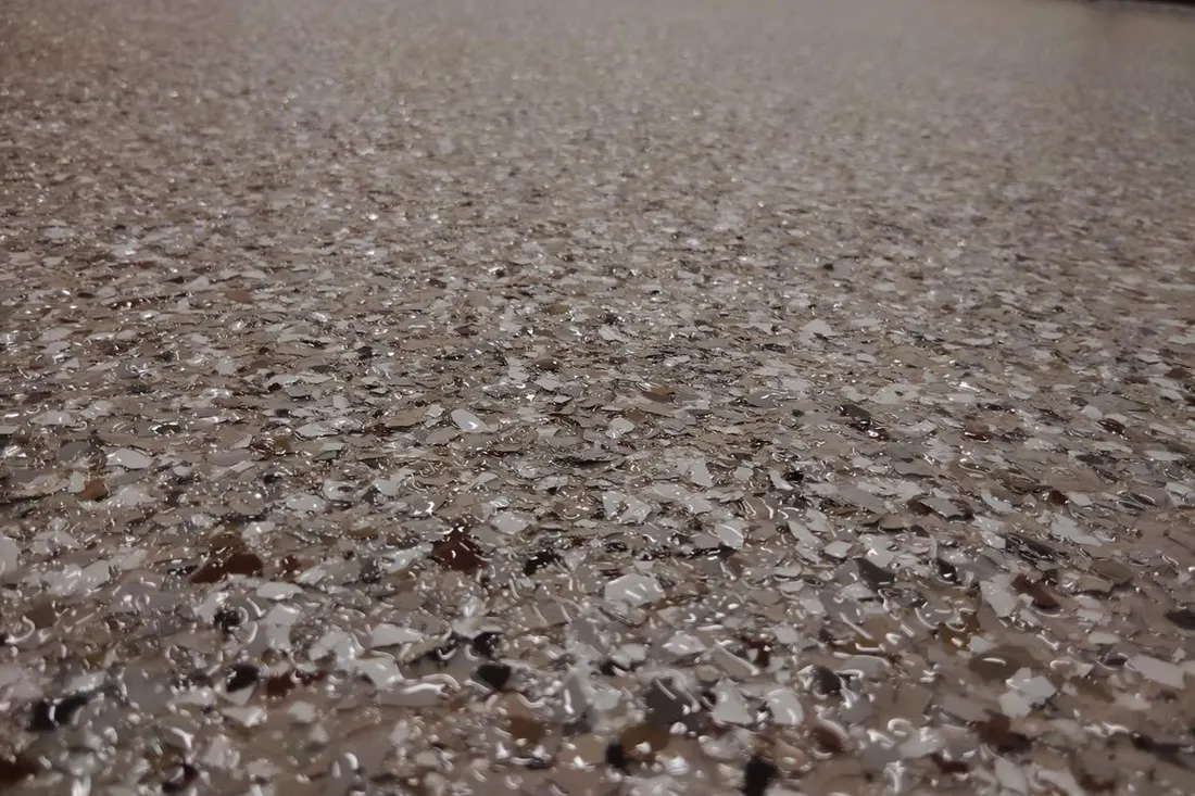 Close-up of a glossy garage floor coating embedded with beige, grey, and white flecks