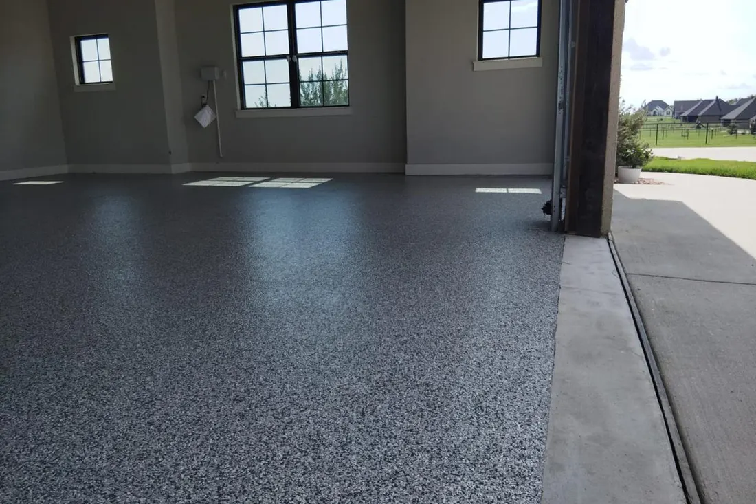 Spacious garage interior featuring a glossy gray speckled flake floor coating beside concrete driveway