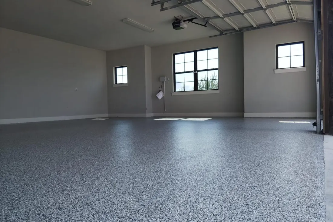 Spacious empty garage interior featuring a gray speckled epoxy coated floor and white walls