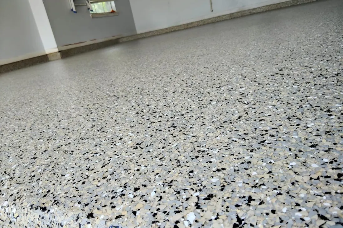 Grey, black, and white speckled epoxy flake coating on an empty garage floor