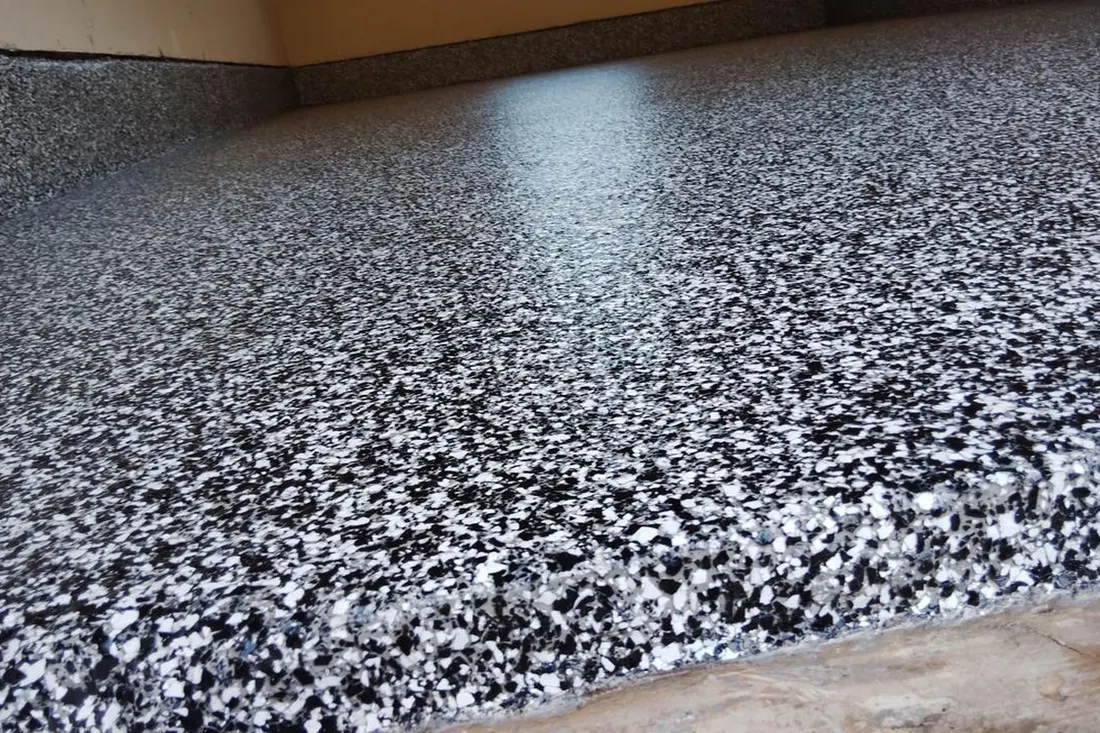 Glossy black, gray, and white speckled epoxy coating on a concrete garage floor and baseboard