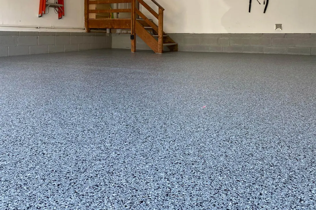 Grey speckled epoxy coating on a spacious garage floor with wooden stairs in background