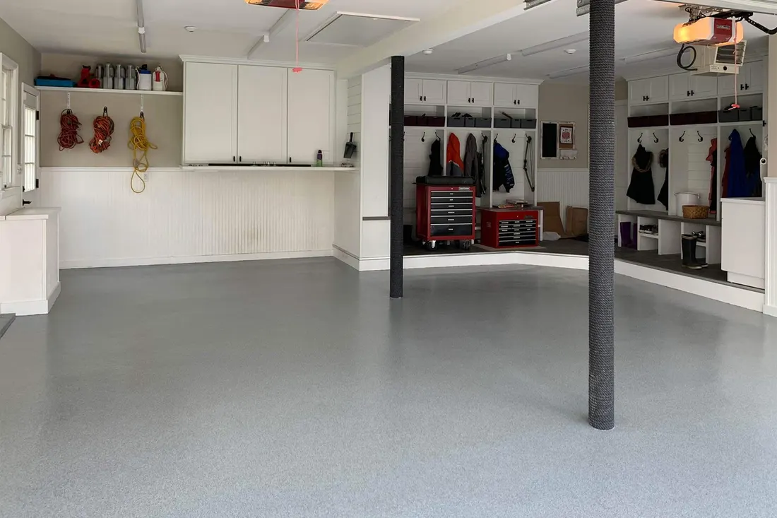 Spacious garage featuring glossy light gray epoxy coated concrete floors and white storage cabinetry