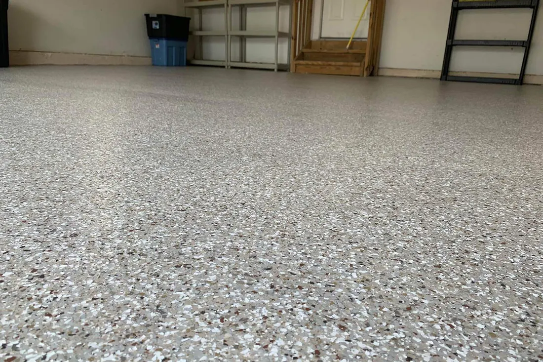 Speckled gray garage floor coating with decorative flakes extending toward shelving and wooden steps