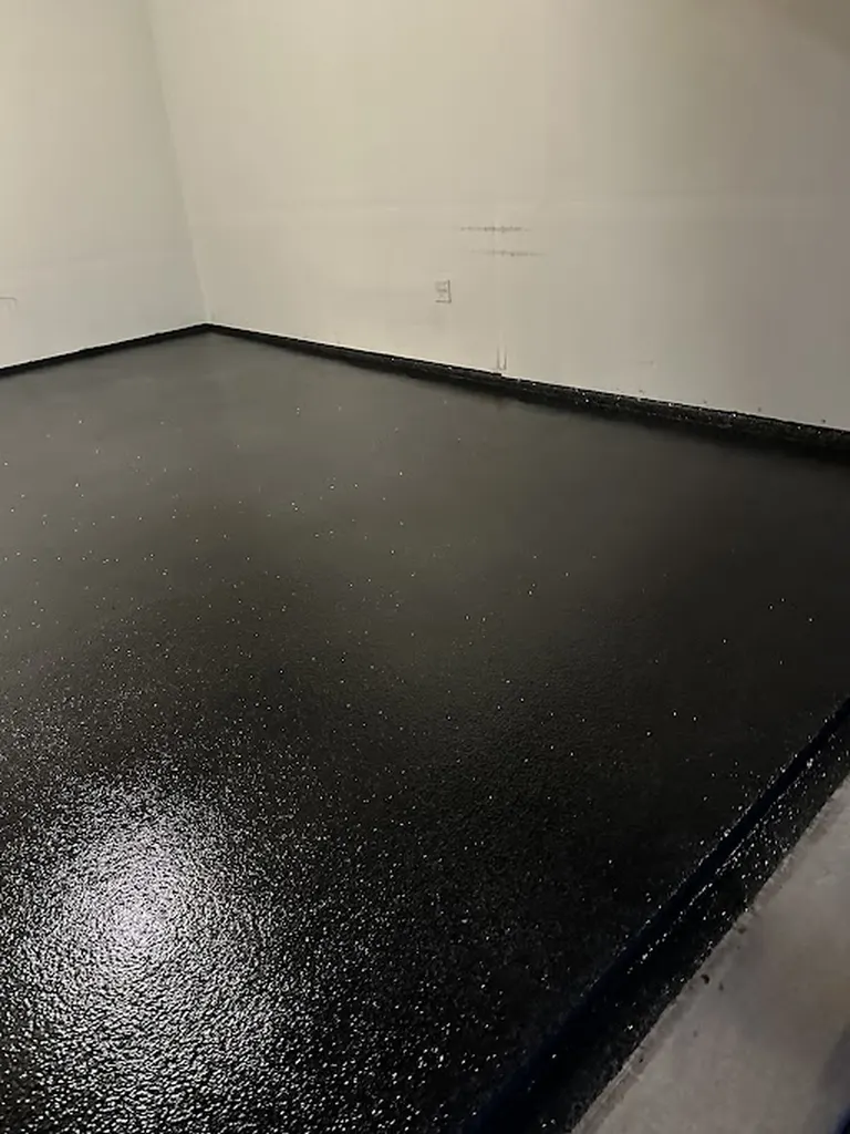 Glossy black coated garage floor with speckled flakes bordered by plain white walls
