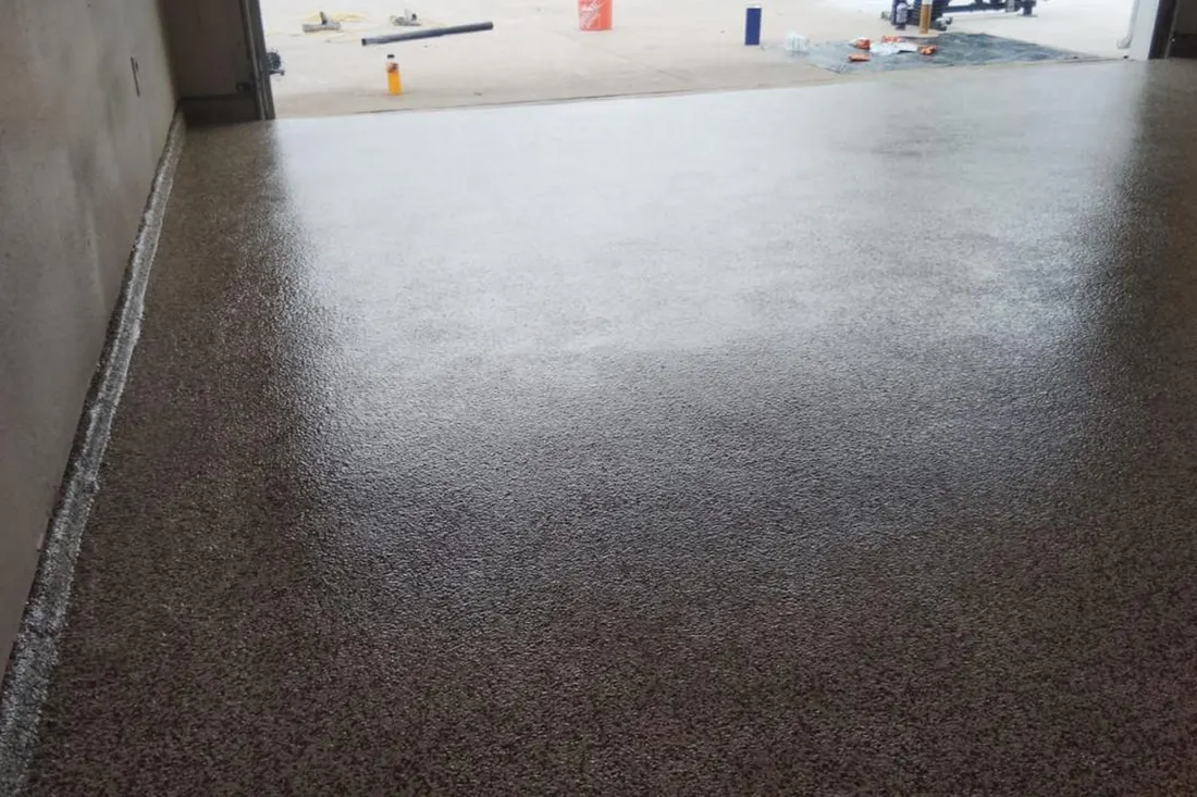 Glossy speckled brown epoxy coating applied to a concrete garage floor leading outdoors
