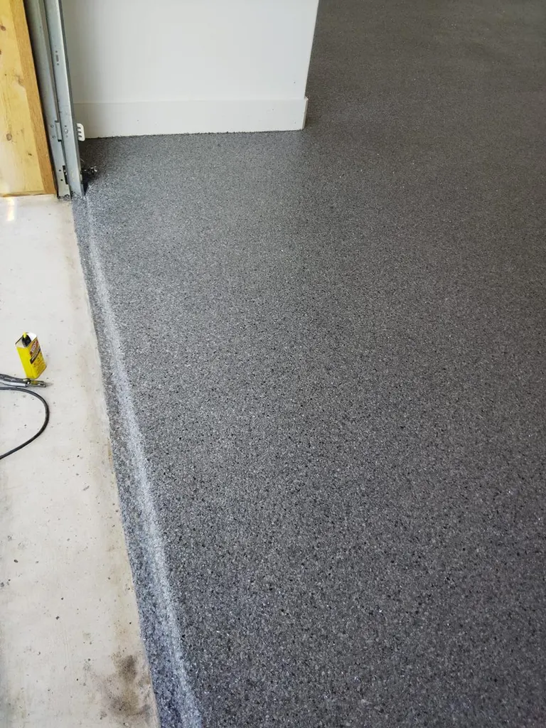 Dark gray speckled epoxy garage floor coating alongside a white wall and doorway threshold