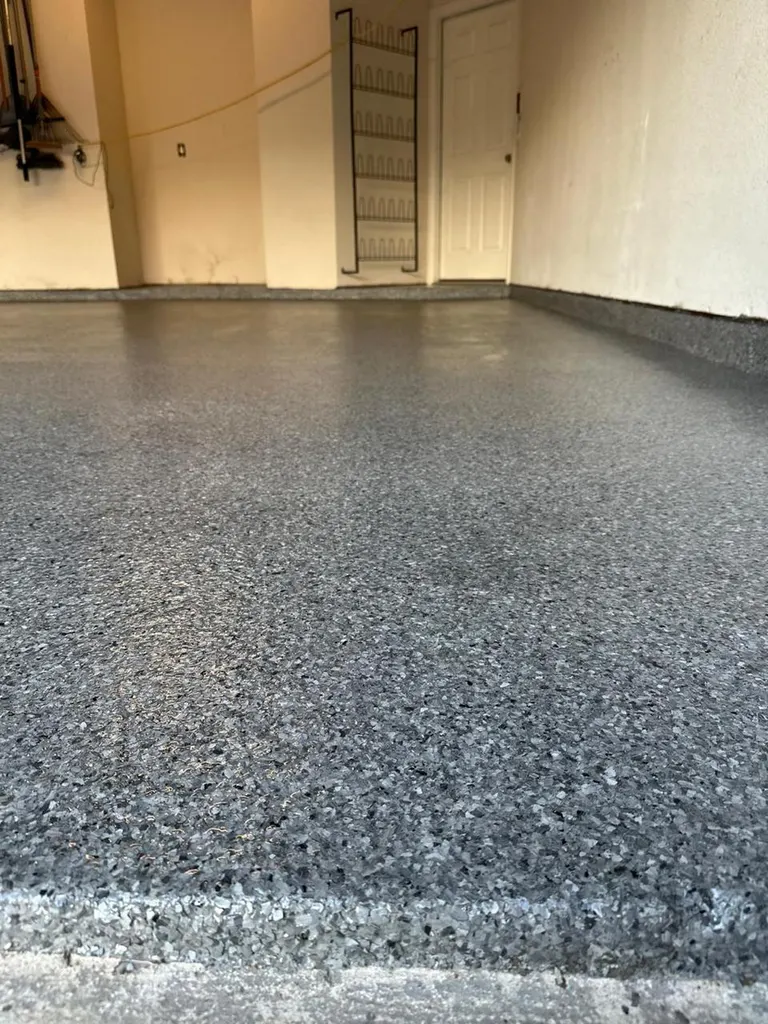 Speckled dark gray epoxy flake coating applied across a concrete garage floor and baseboards