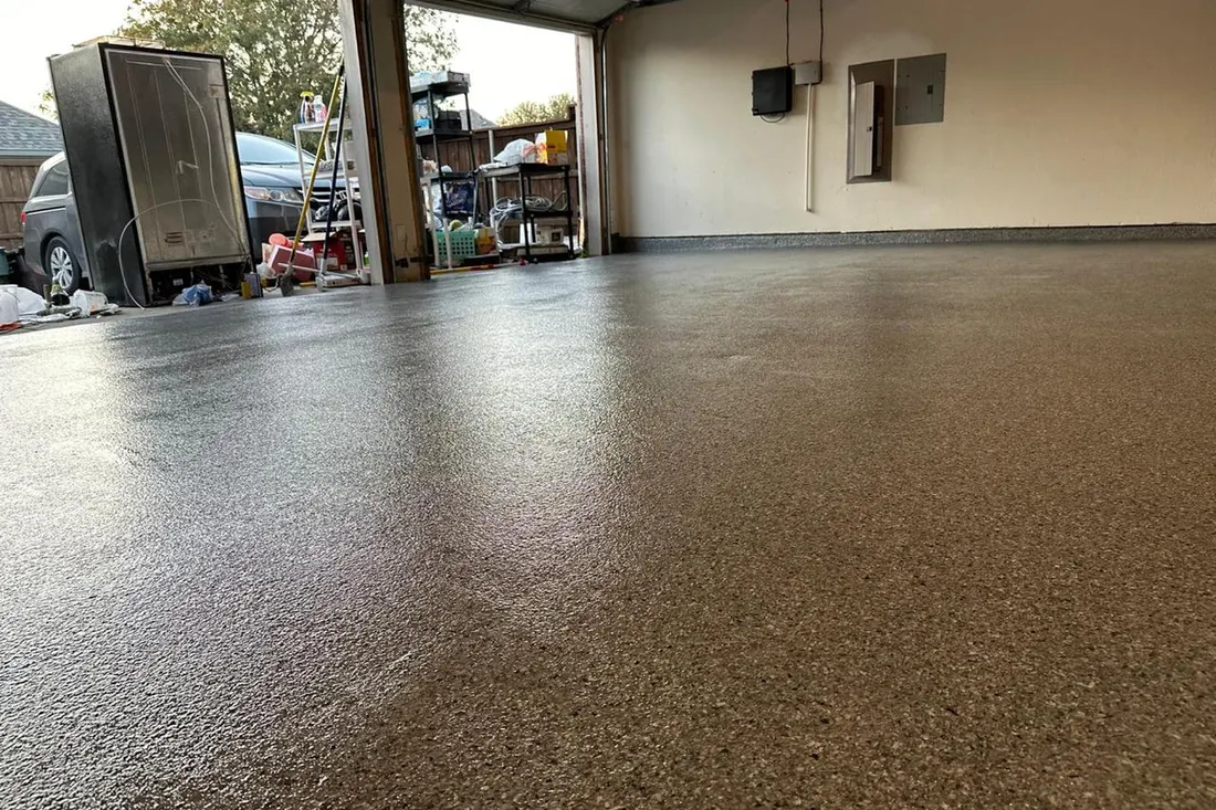 Glossy speckled tan epoxy coating on a residential garage floor with open bay door