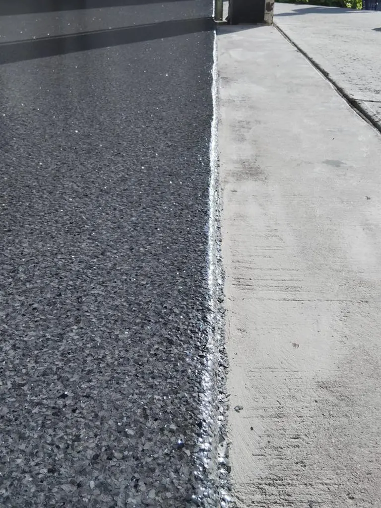 Glossy dark gray flecked garage floor coating bordering an unfinished concrete threshold