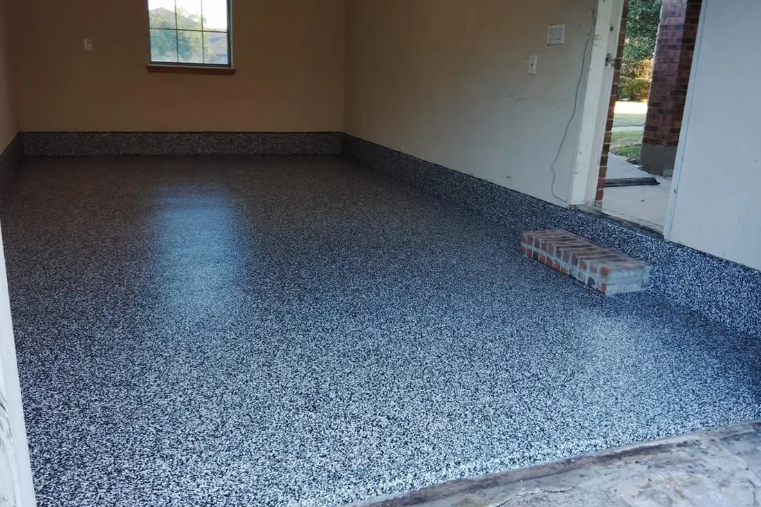 Empty garage interior with glossy speckled gray epoxy floor coating extending up baseboards